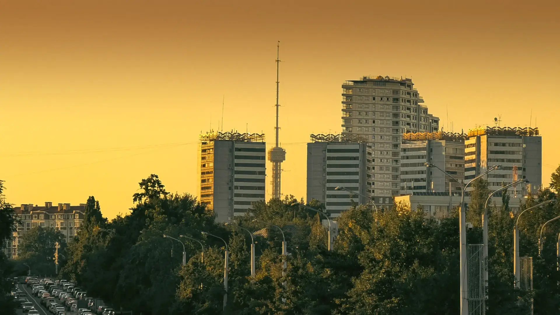 Kechki Toshkent: oltin rang shafaq fonida Tashkent City va teleminora, mashinalar bilan toʻla shoh koʻcha